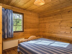 Una habitación de cabaña de madera con una cama, una ventana con cortinas y una lámpara en el techo.