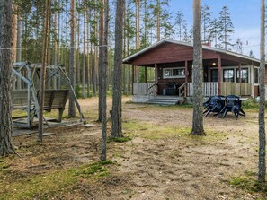 Une cabane dotée d’un porche et de meubles de jardin, entourée d’une forêt.