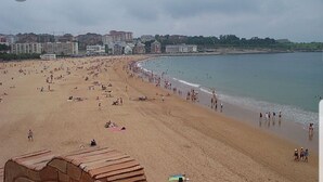 Une plage très fréquentée, avec une étendue de sable et des bâtiments visibles à l’arrière-plan.