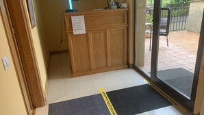 Un espace d’accueil avec un bureau en bois, un panneau indicateur et une porte vitrée donnant sur l’extérieur.