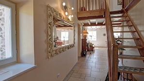 A staircase with wooden railings leading to an upper floor, a large ornate mirror with lights above it, and a stone-framed window on the left.