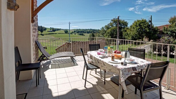 A balcony with a table set for breakfast, overlooking a rural landscape.