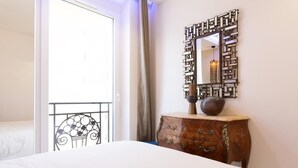 Une chambre d’hôtel avec un lit, une commode en bois, un miroir décoratif et une vue sur le balcon extérieur.