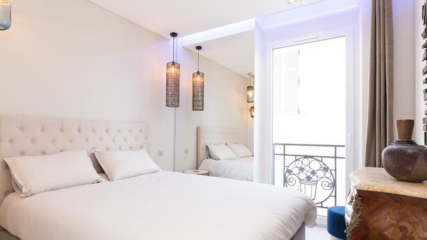 Une chambre à coucher avec un grand lit, un miroir, une table de chevet en bois et un balcon doté d’une balustrade.