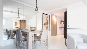 Un espace repas moderne avec une table et des chaises en bois, un luminaire suspendu et une œuvre d’art encadrée au mur.