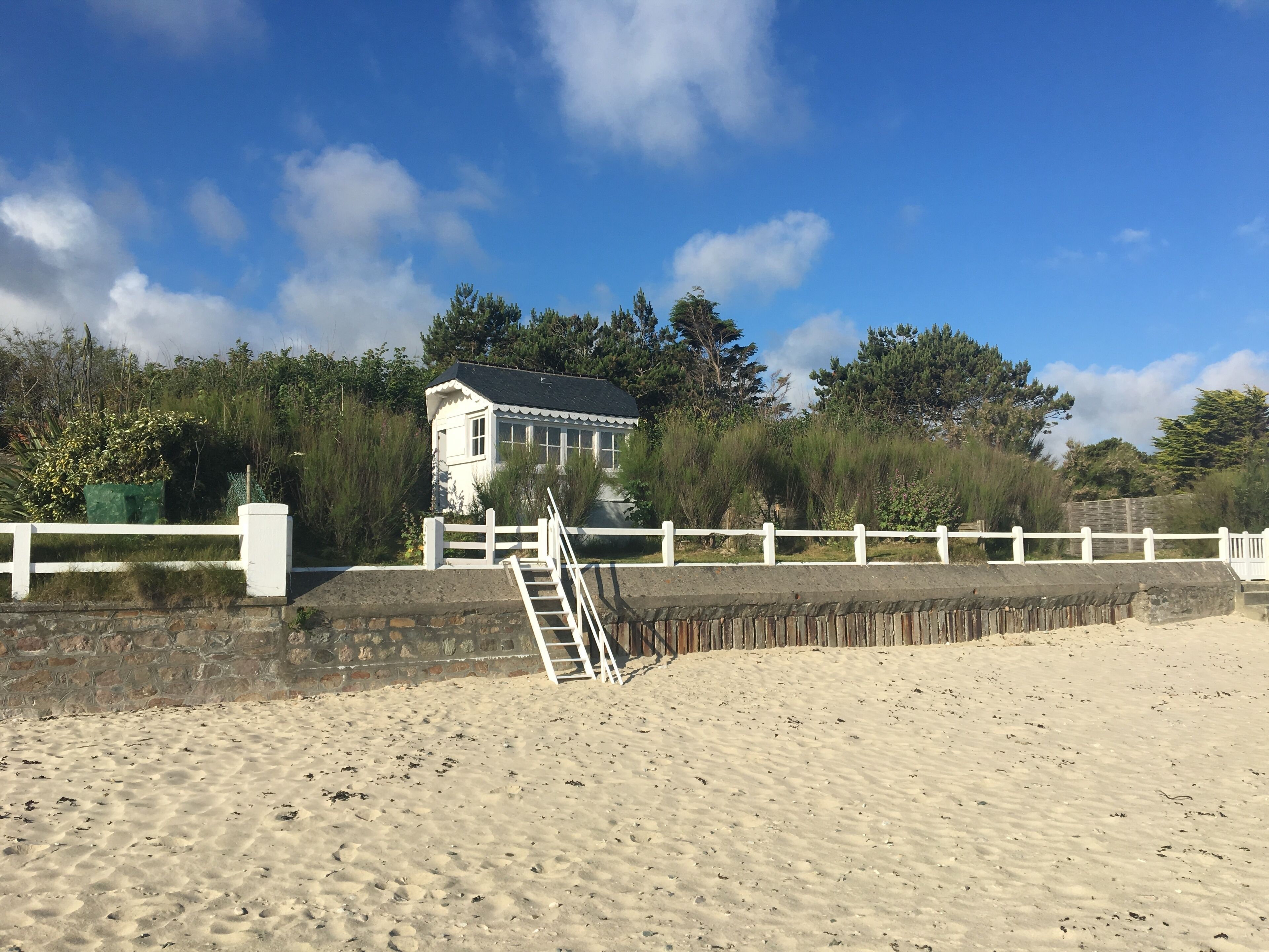 A beach house with a white exterior, a stone wall, and a white fence.