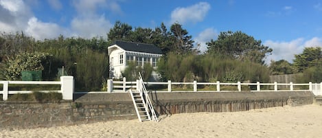 Une maison de plage à l’extérieur blanc, avec un mur en pierre et une clôture blanche.