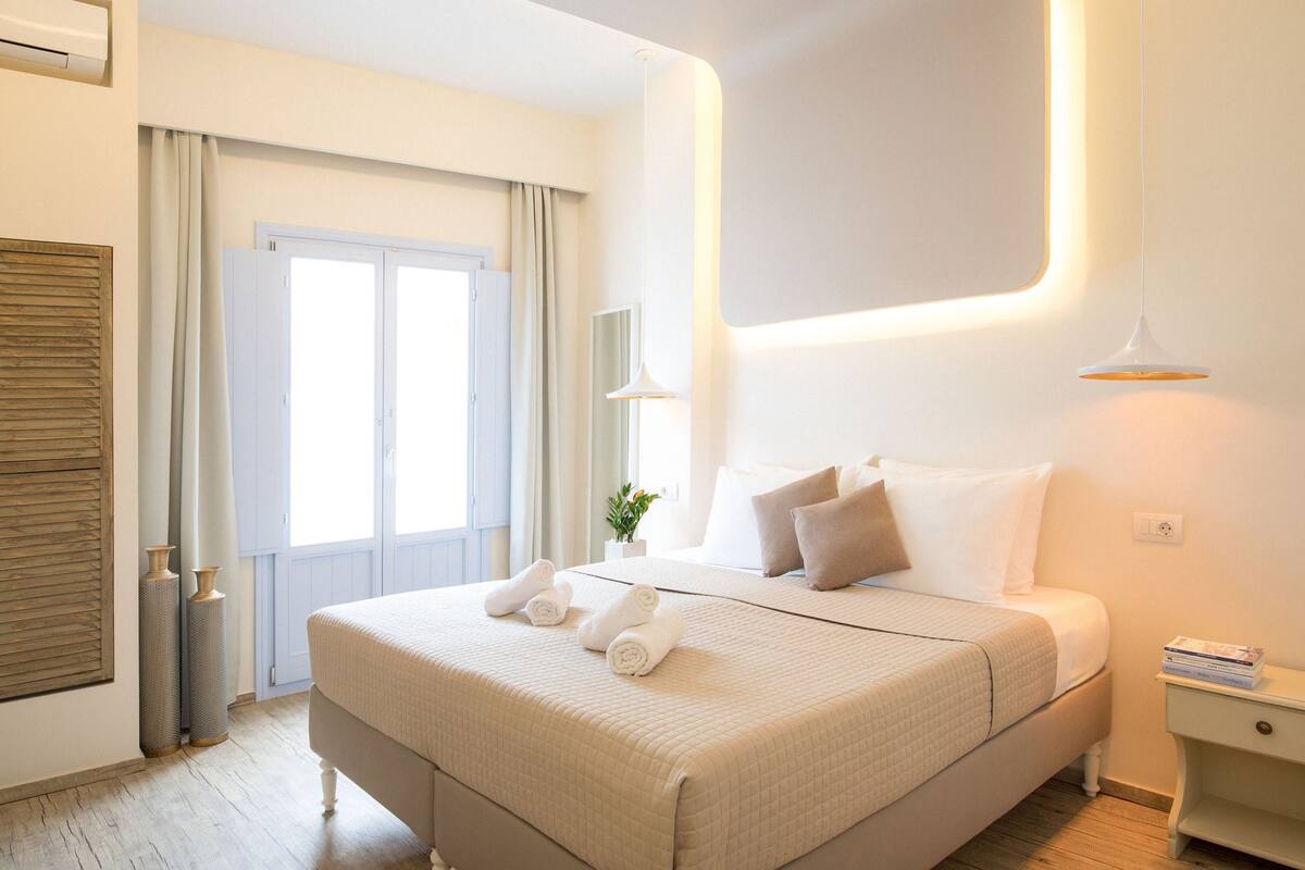 A neatly arranged hotel room with a large bed, a bedside table with a lamp, and a view through a door.