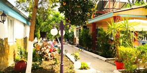 A narrow street with buildings on either side, a small garden area with potted plants, and a street lamp. - Side Erenler Hotel (Manavgat)