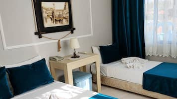 Habitación de hotel con dos camas, una mesita con lámpara, un cuadro en la pared y una ventana con cortinas.
