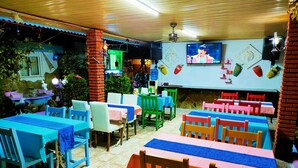 Een restaurant met meerdere tafels en stoelen, een aan de muur bevestigde televisie en een decoratieve fontein.