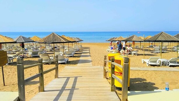 Een strand met ligbedden en parasols, een houten looppad naar het strand en een redershut.