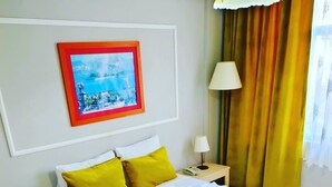 Een hotelkamer met een groot bed, twee nachtkastjes met lampen, een lijst met een afbeelding aan de muur, en een raam met gordijnen.