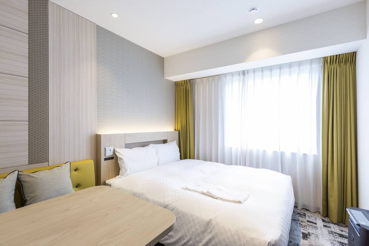 Habitación de hotel con una cama grande, una mesita de noche, un escritorio y una ventana con cortinas.