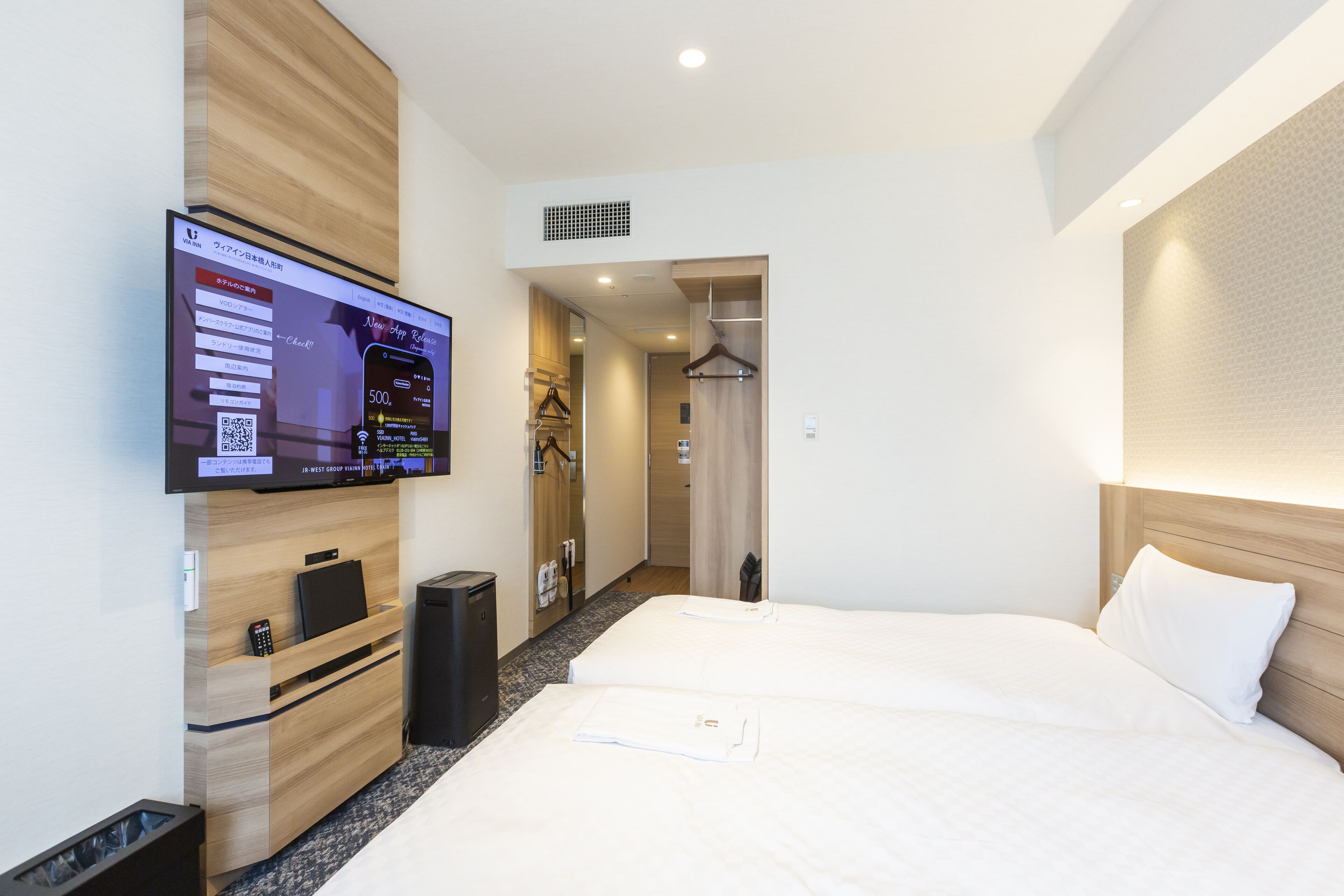 A hotel room with a bed, a TV mounted on the wall, a desk with a computer, and a wardrobe.