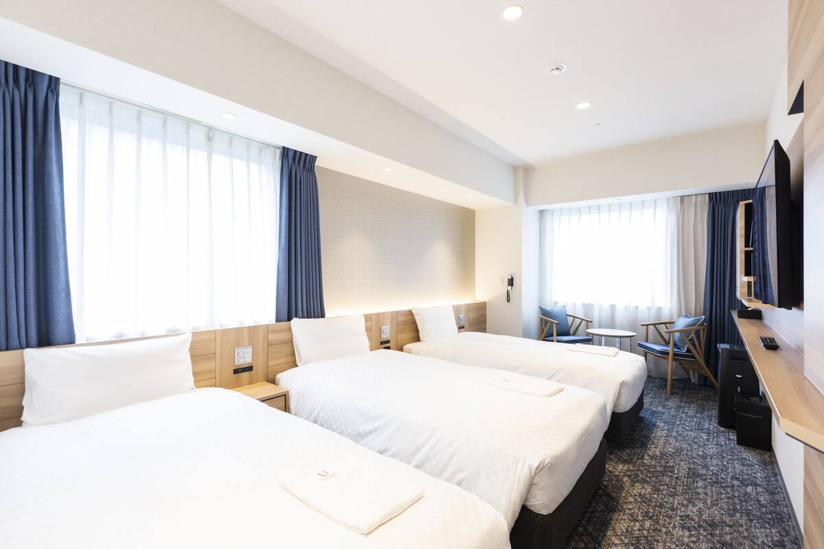 Habitación de hotel con tres camas, un escritorio, una silla y un televisor.