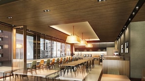Een moderne eetruimte met lange tafels en stoelen, een keuken en grote ramen met uitzicht op de stad.