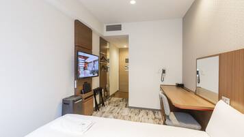 A compact hotel room with a bed, a desk, a chair, a television, and a small kitchenette.