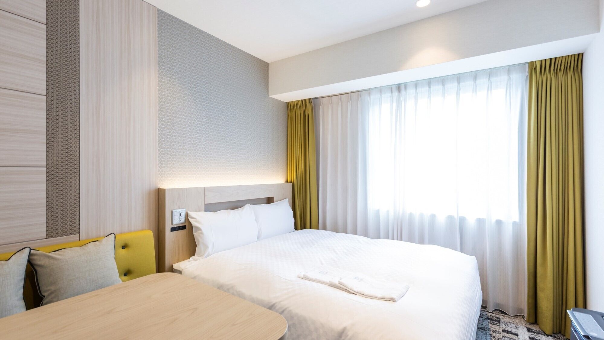 A hotel room with a bed, a desk, and a window with curtains.