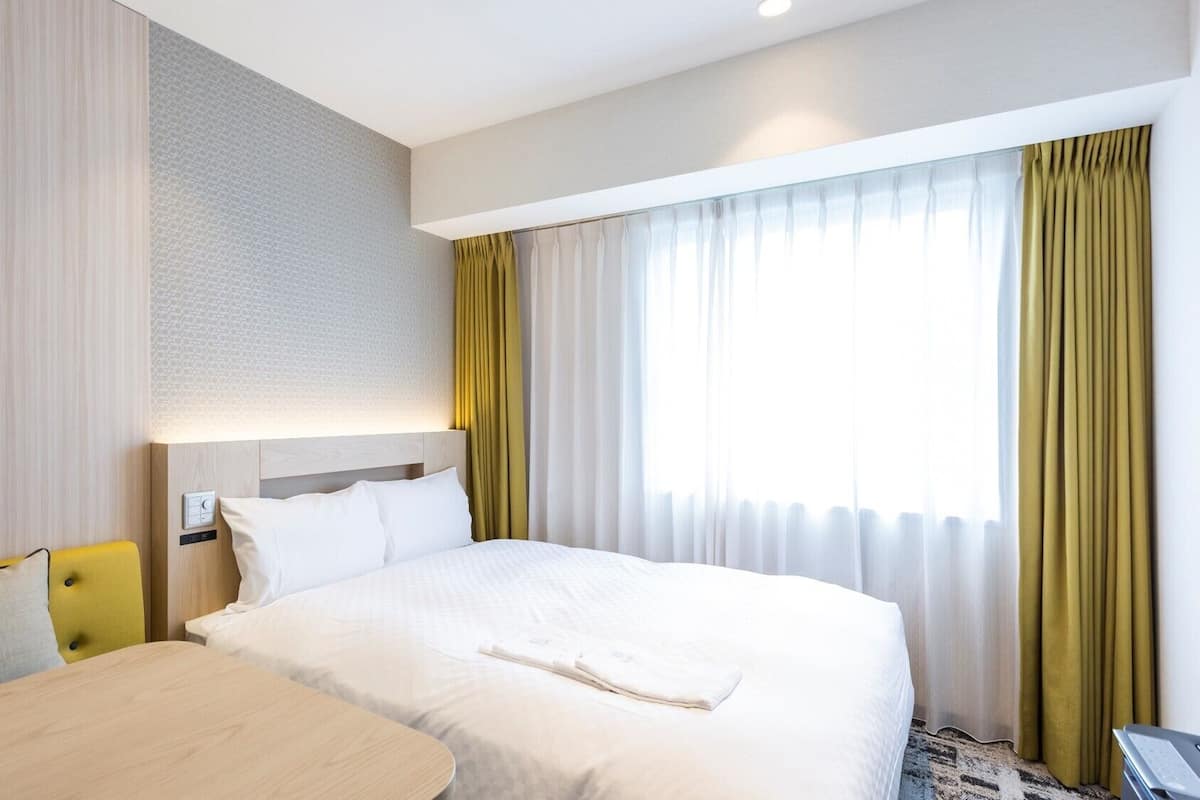 Una habitación de hotel con cama, escritorio y ventana con cortinas.