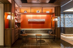 Eine moderne Hotelhalle mit einer Couch, zwei kleinen Tischen und Holzregalen mit Büchern und Dekorationsobjekten.