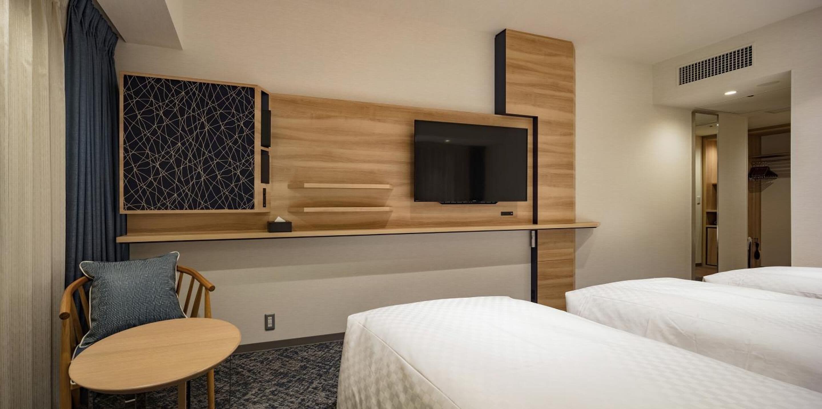 A hotel room with a bed, a desk, a chair, a TV mounted on the wall, and a wardrobe.