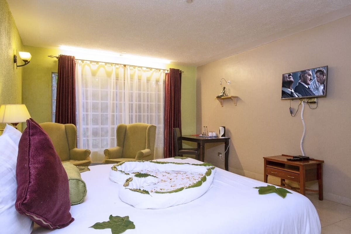 Hotellihuone, jossa on sänky, tuoli, työpöytä, televisio ja ikkuna, jossa on verhot.