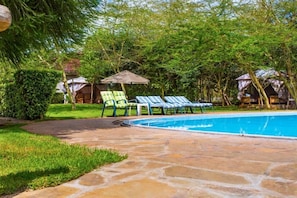 A swimming pool with lounge chairs and umbrellas, surrounded by greenery and trees. - Lukenya Motorcross (Athi River)