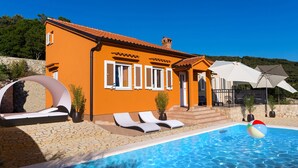 A villa with a swimming pool, white shutters, and a stone wall.