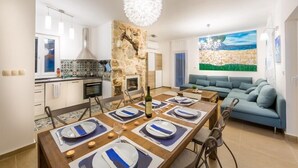 A modern kitchen with a stone wall, a dining area set for six with blue and white tableware, and a blue sofa in a bright living room with a beach mural.