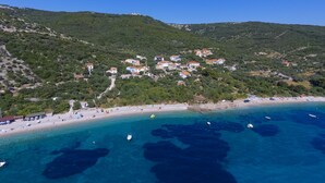 An aerial view of a coastal town with buildings on a hillside, a beach, and boats in the water.