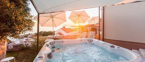 A hot tub under a canopy with a view of the sunset and lounge chairs.