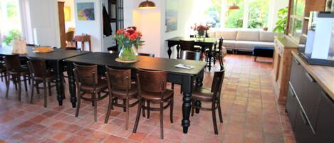 A dining area with a large table and chairs, a vase with flowers, and a kitchen area with cabinets and a refrigerator.