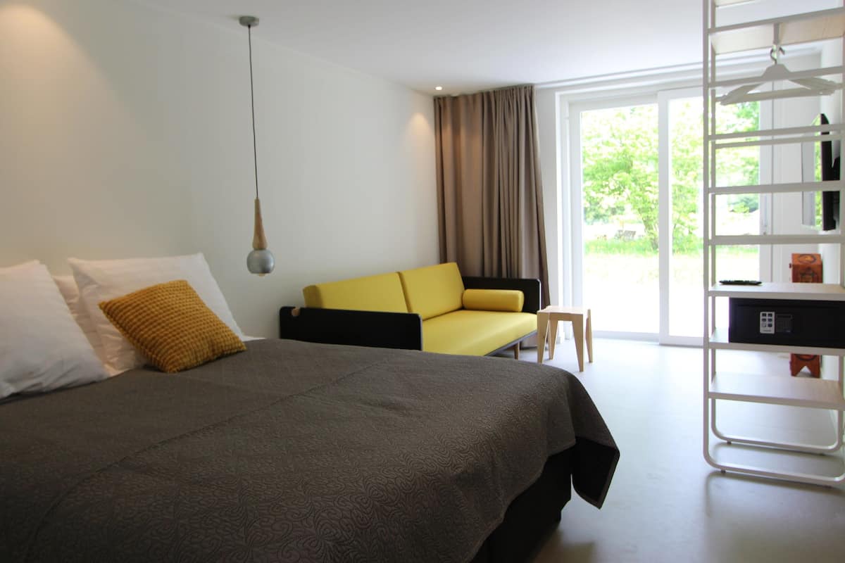 A modern hotel room with a large bed, a sofa, and a desk with a computer.