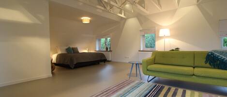 A spacious attic bedroom with a large bed, a green sofa, and a colorful striped rug.