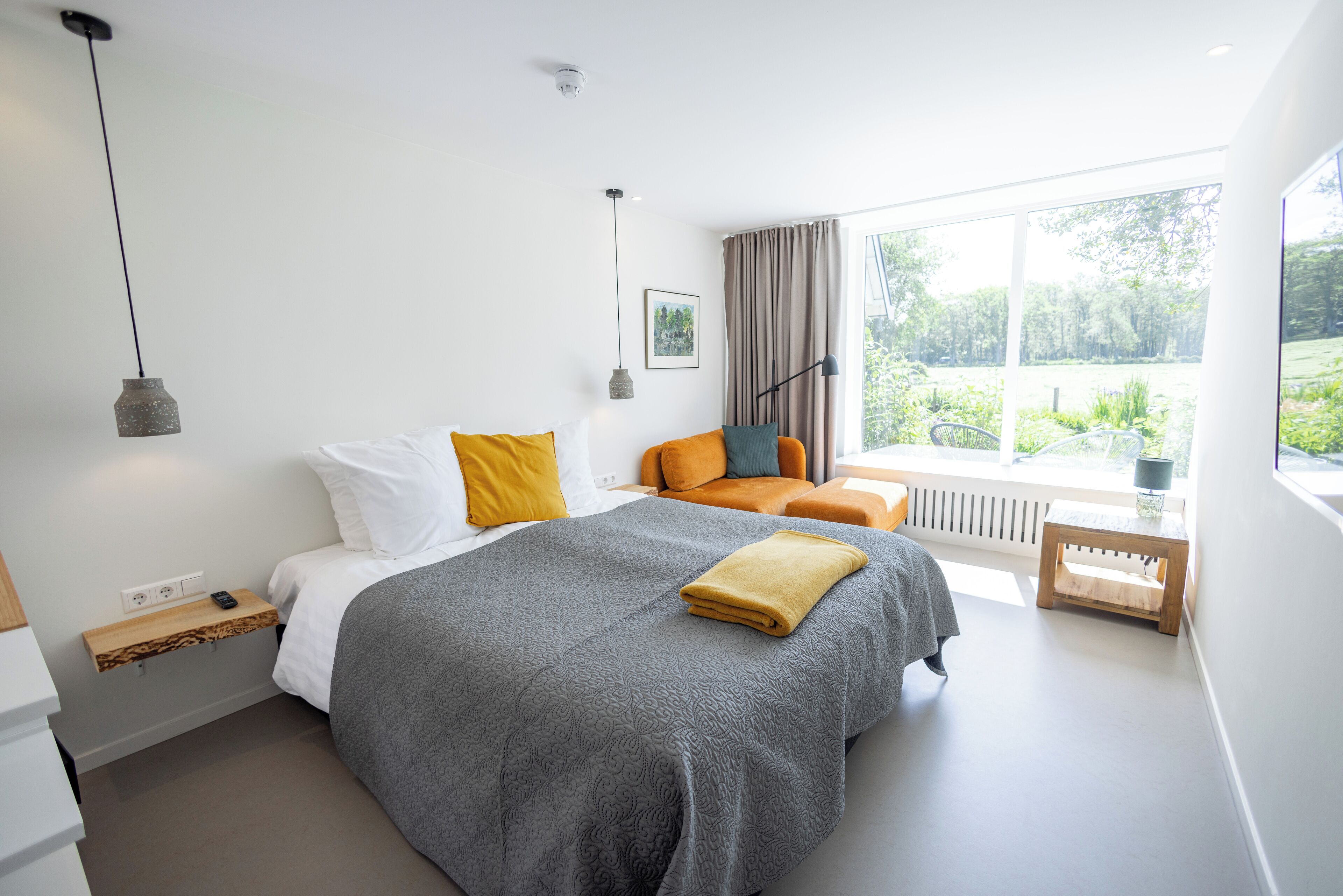 Un dormitorio moderno con una cama grande, una mesita y una ventana con vistas a zonas verdes.