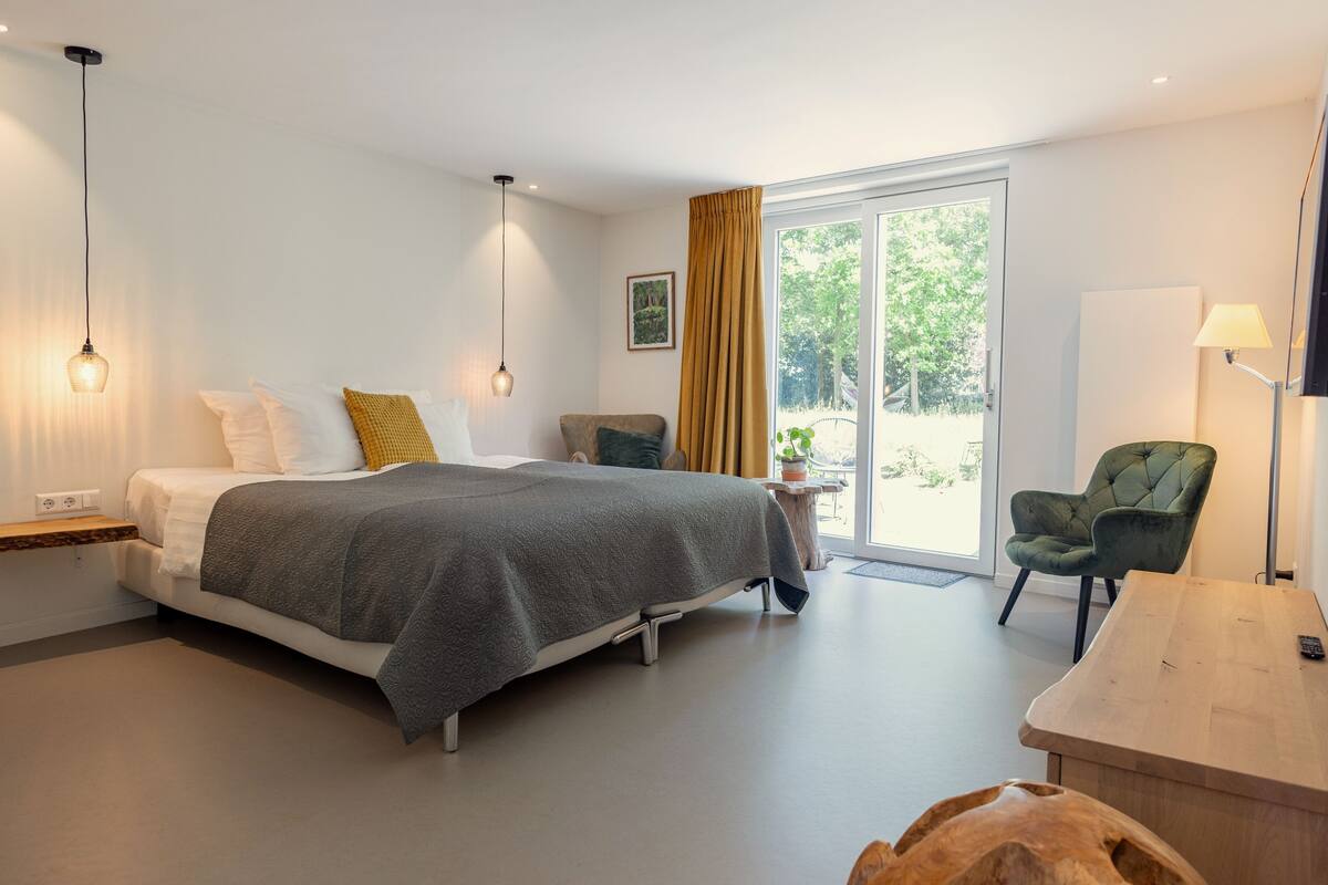 A modern bedroom with a bed, bedside table, lamp, chair, and a view of the outdoors.