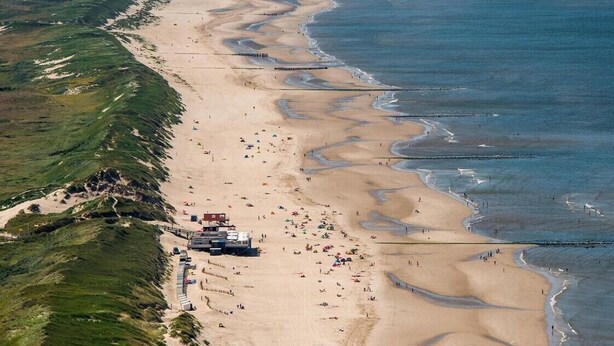 Luchtbeeld van een strand met mensen, parasols en een wachthuisje.