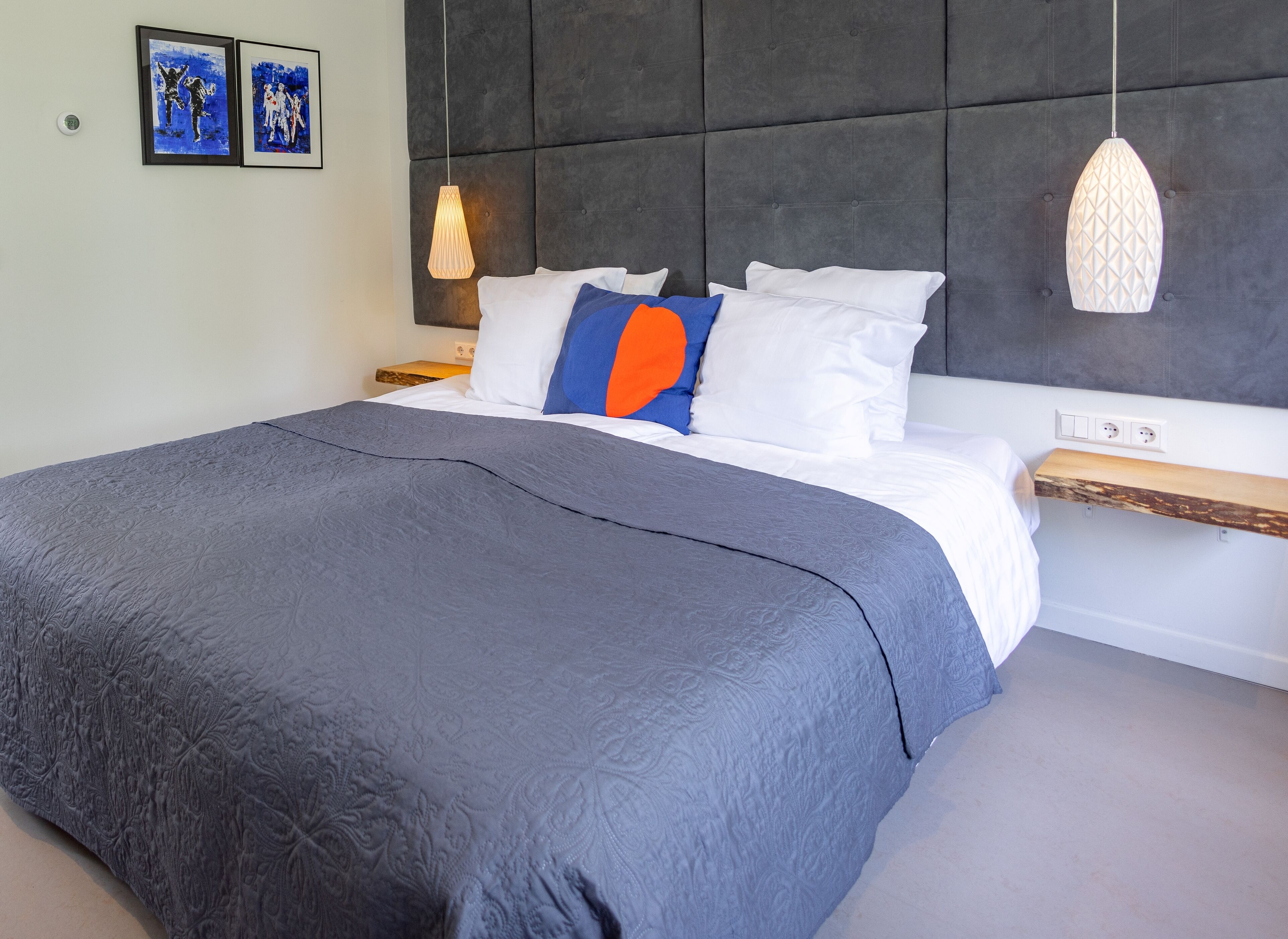 A modern bedroom with a large bed, grey textured headboard, white bedding, and a wooden nightstand.