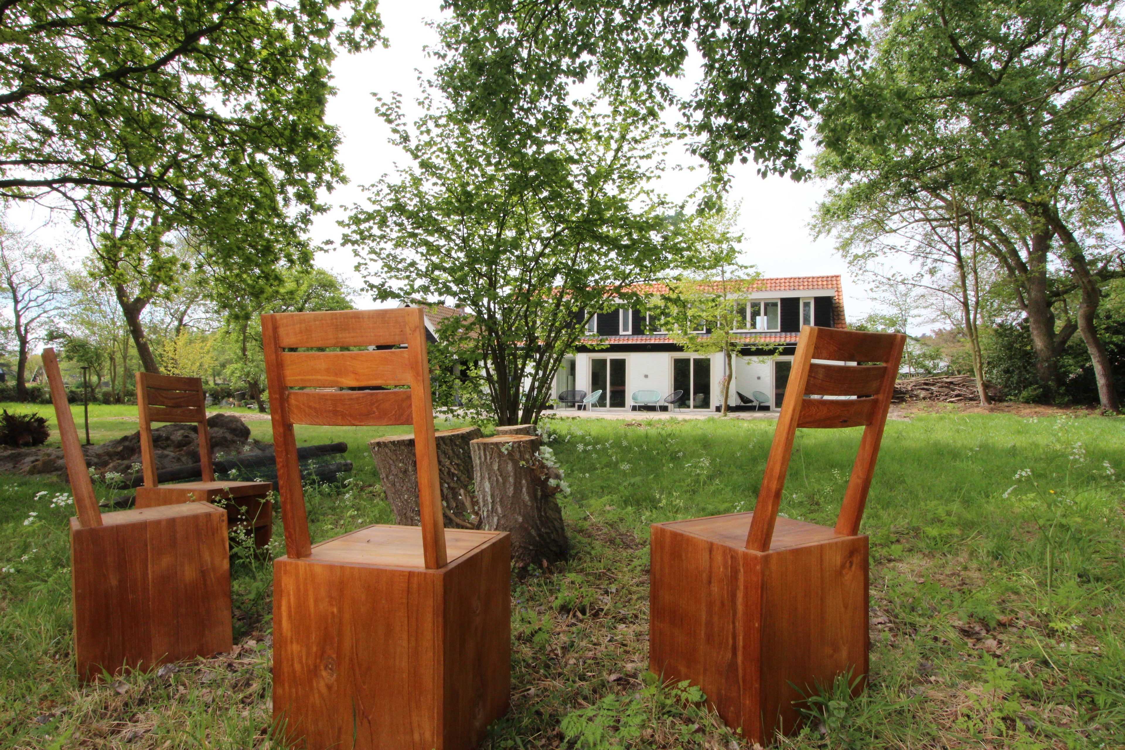 Three wooden chairs with backrests and seats placed on a grassy area with trees and a building in the background.