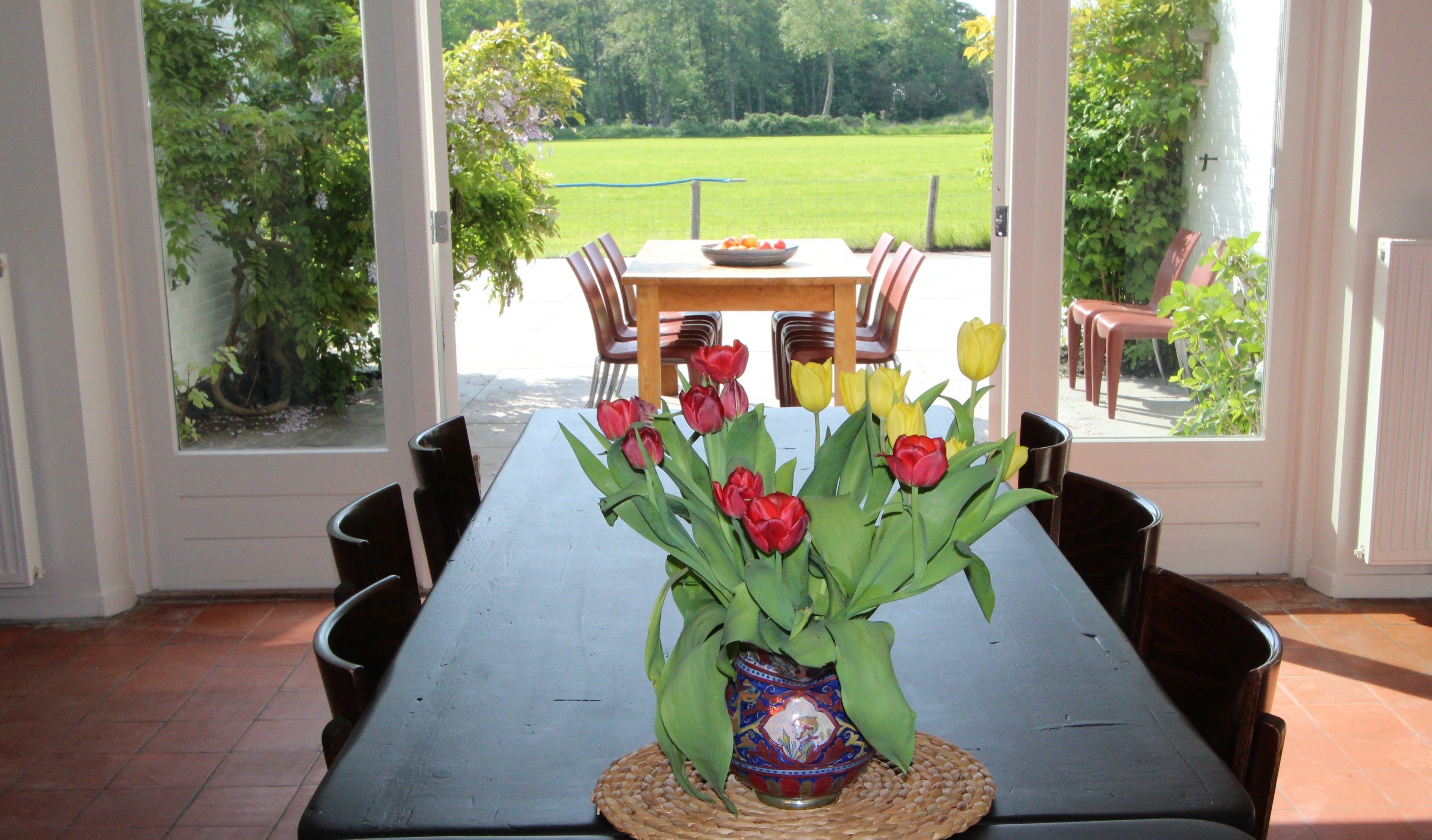 Una mesa de comedor con un jarrón de tulipanes en el centro, rodeada de sillas.