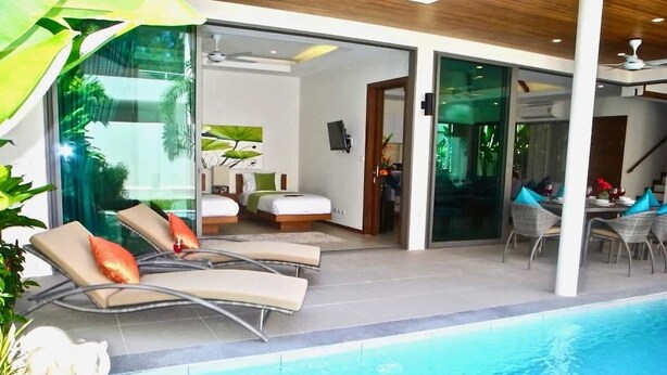 A modern hotel room with a pool, two sun loungers, a dining area, and a staircase leading to another level. - Rawai Ka 3 Bedroom Villa (Rawai)