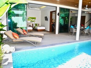 A modern hotel room with a pool, two sun loungers, a dining area, and a staircase leading to another level. - Rawai Ka 3 Bedroom Villa (Rawai)