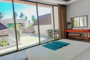Ein Hotelzimmer mit einem großen Bett, einem Schreibtisch, einem Stuhl und einem Balkon mit Blick auf Palmen und ein Gebäude.