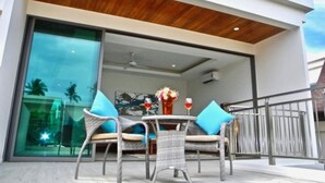 A modern outdoor seating area with wicker chairs and a glass table, overlooking a pool and a building with a wooden ceiling. - Rawai Ka 3 Bedroom Villa (Rawai)