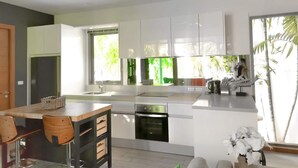 A modern kitchen with white cabinets, a central island, and a dining area with wooden chairs. - Rawai Ka 3 Bedroom Villa (Rawai)