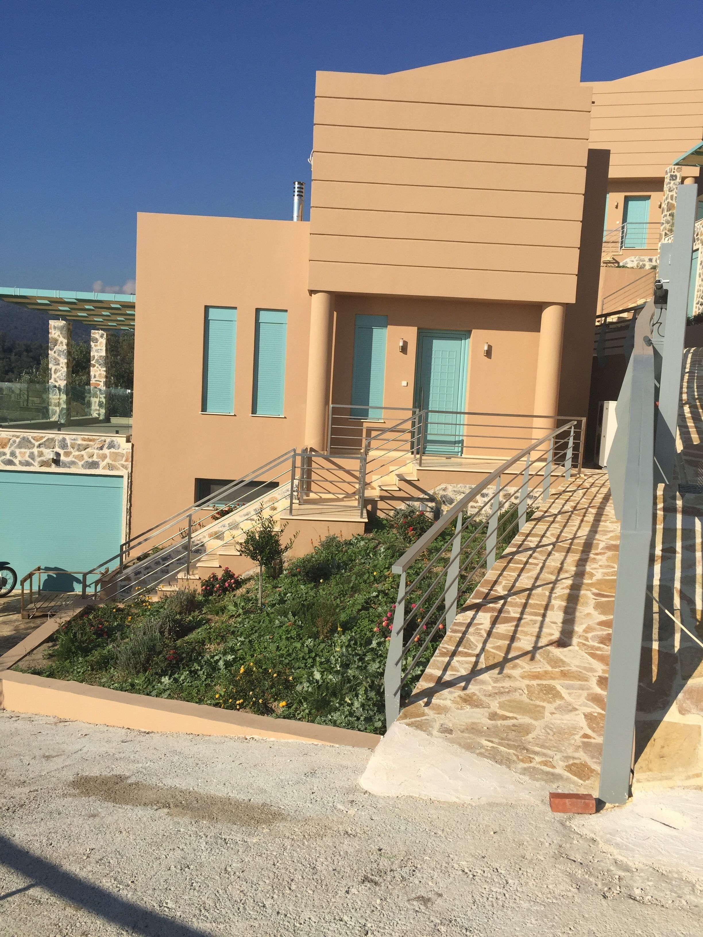 A modern building with a flat roof, a staircase leading to a door with a blue shutter, and a pool in the background.