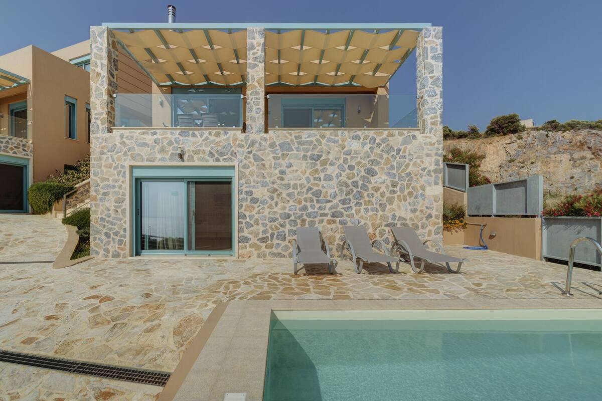 A modern house with a stone facade, a pool, and outdoor seating.