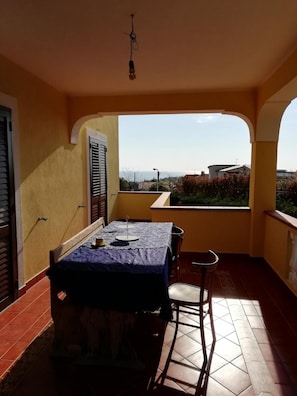 A balcony with a table and chairs, a view of the sea, and a tiled floor.