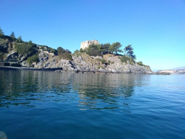 A coastal view with a historic building on a rocky hill, calm water, and clear skies.